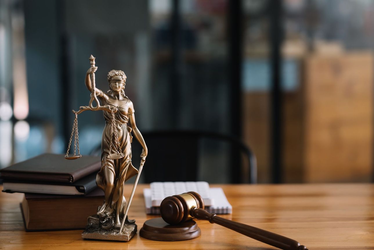A statue of justice is sitting on a wooden table next to a judge's gavel.