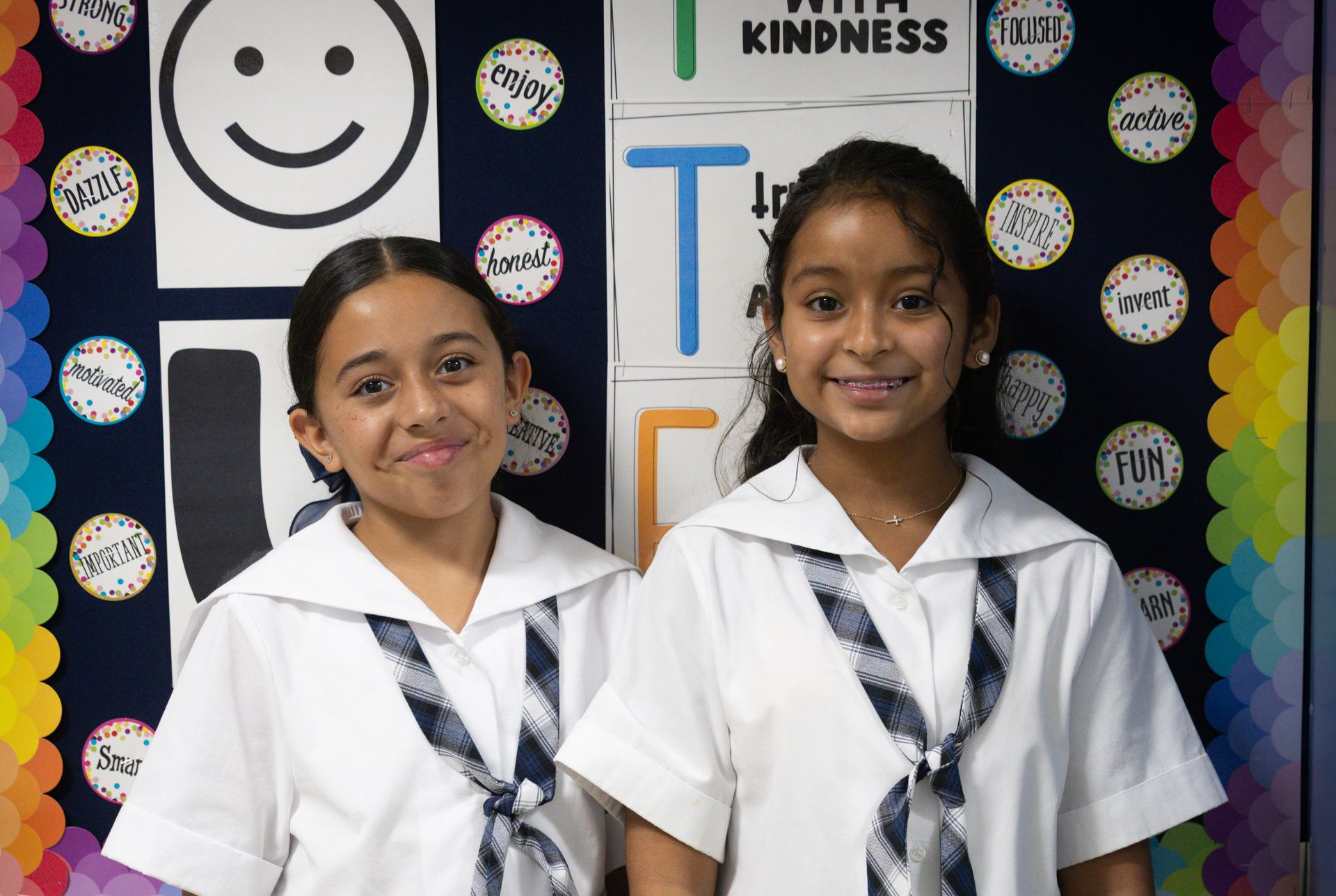 Two girls in school uniforms are standing next to each other and smiling.