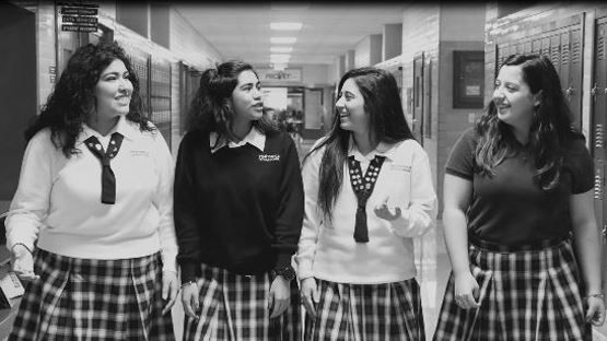 A group of girls in school uniforms are walking down a hallway.