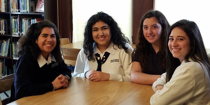 Four girls are sitting at a table and smiling for the camera