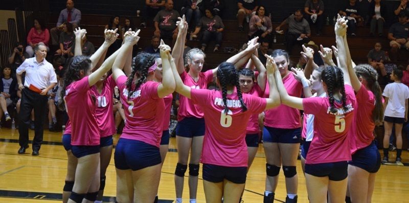A group of girls are standing in a huddle on a volleyball court.