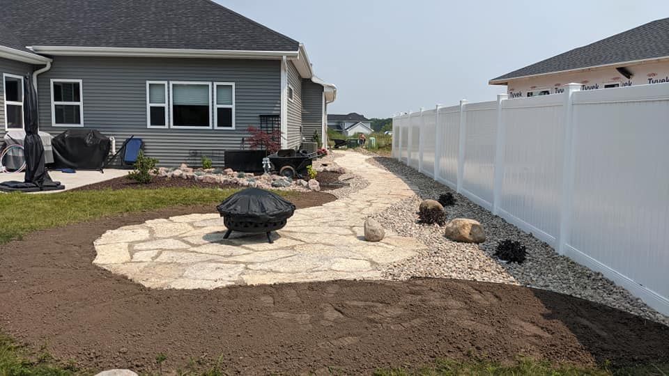 Backyard with stone patio, fire pit, path, white fence, and house.