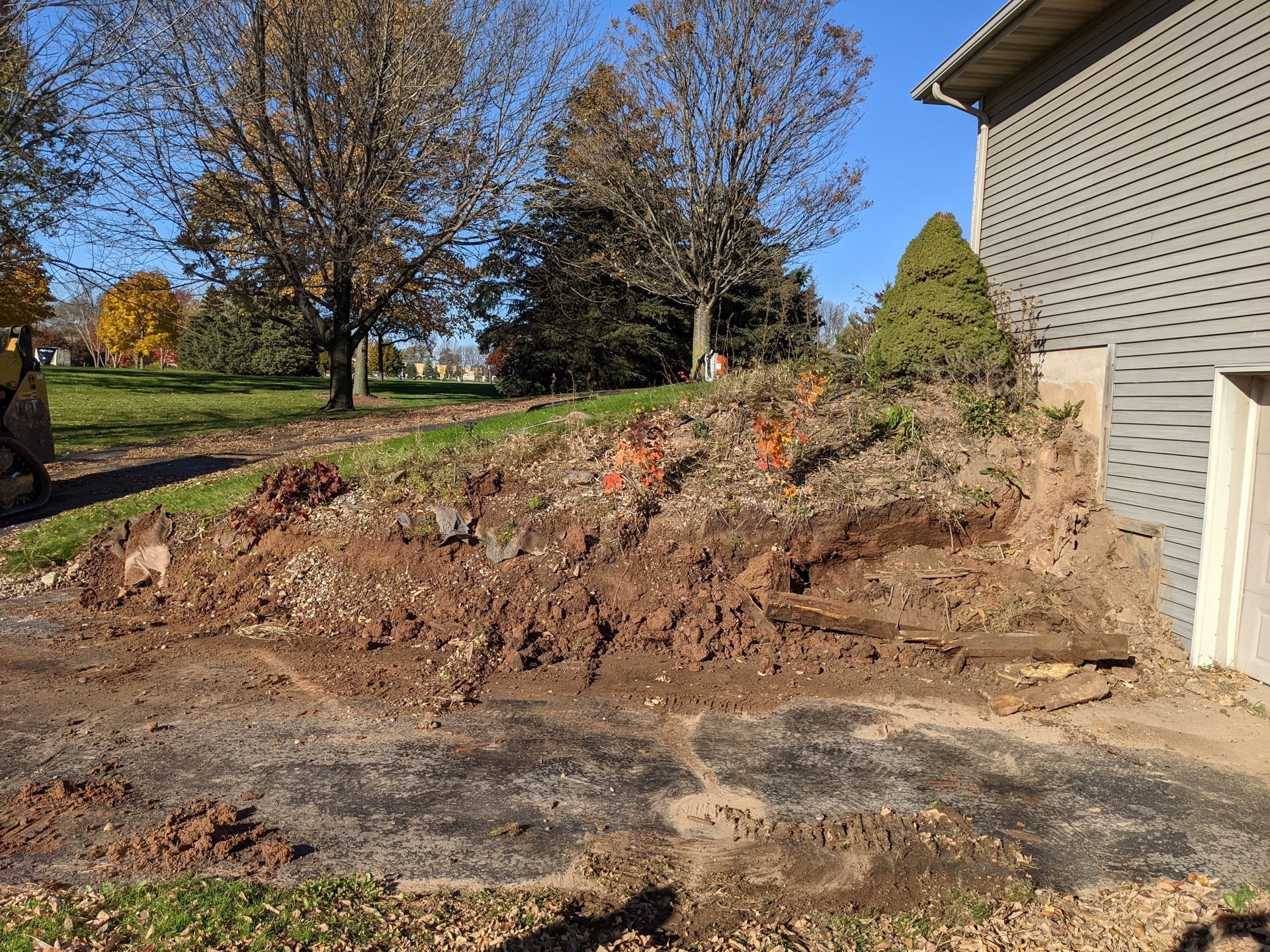 Dirt piled up next to a building's gray siding, in front of trees and grass under a blue sky.