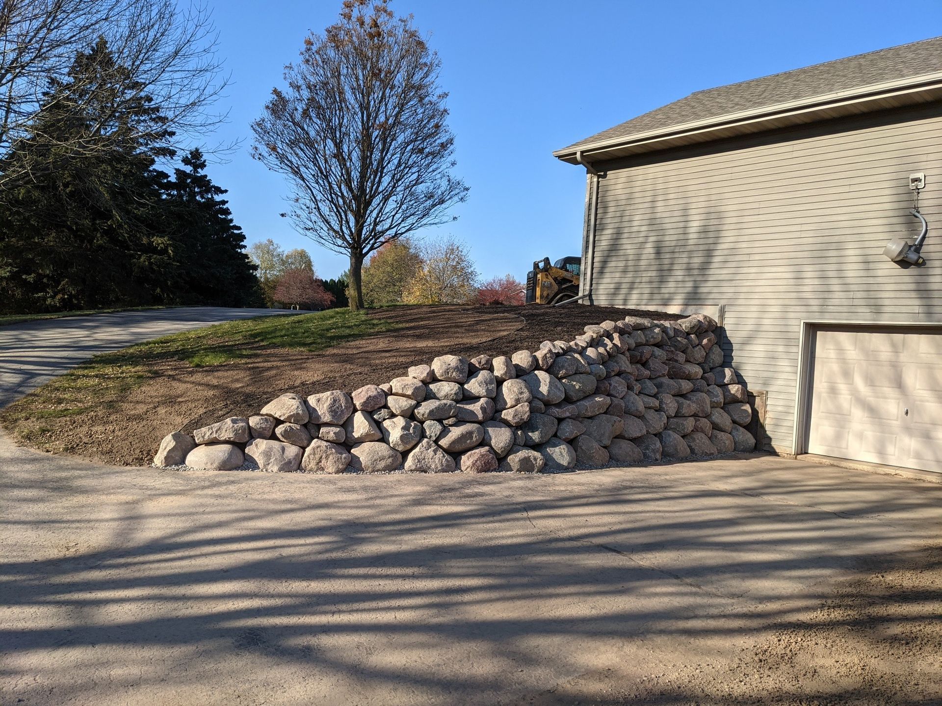 Stone retaining wall next to a beige building with a driveway and blue sky.