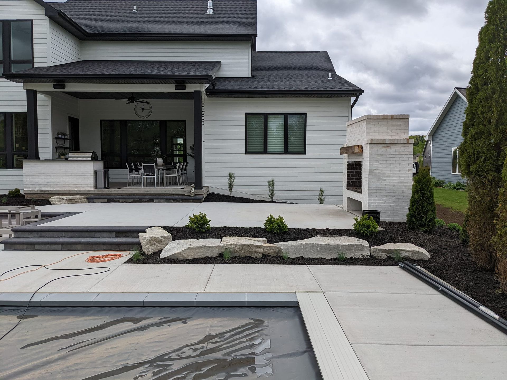 Backyard with pool, patio, and white house with black trim. Fireplace and landscaping visible.