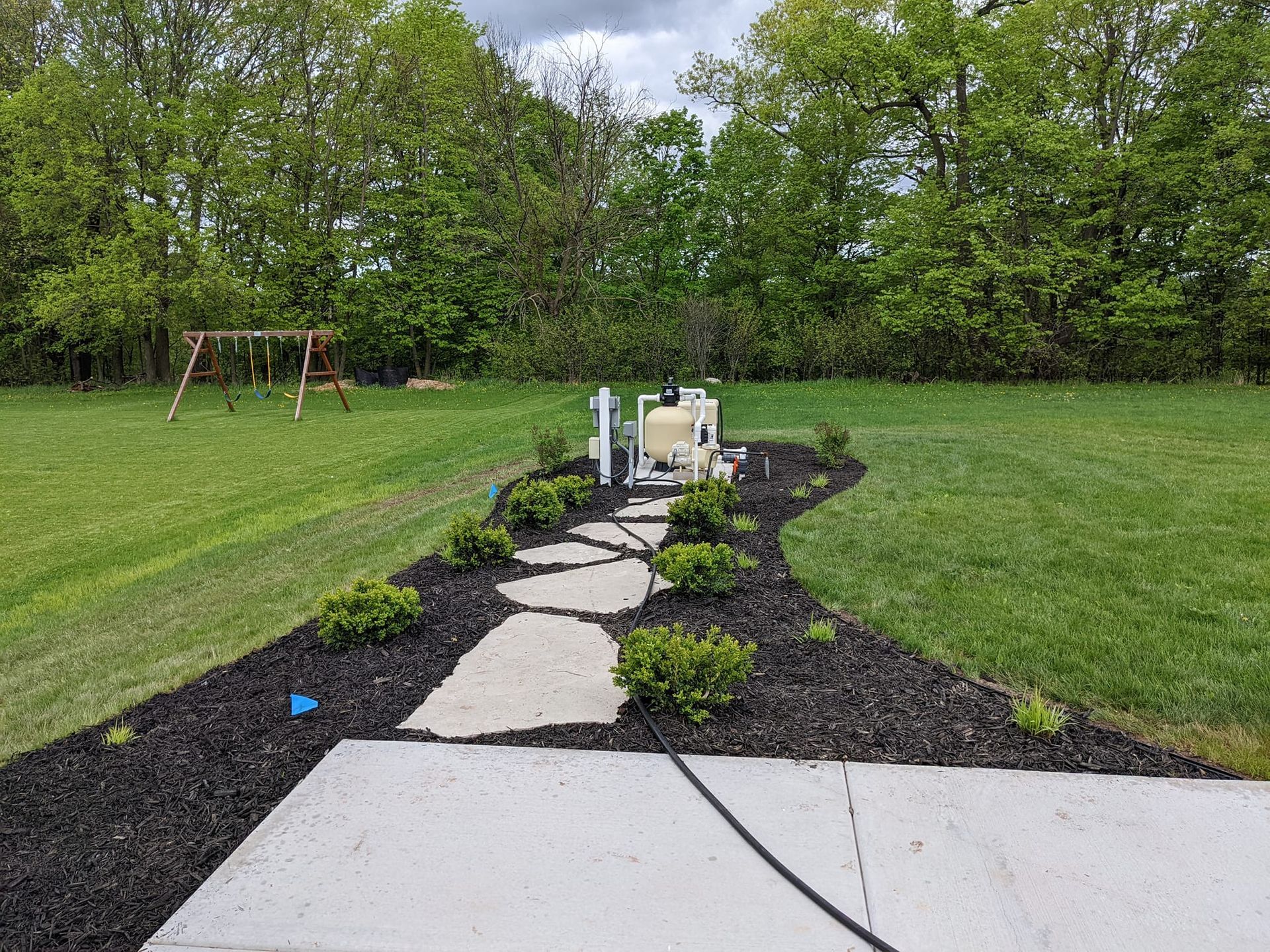 Stone path through landscaped yard leading to equipment, with swing set in the background.