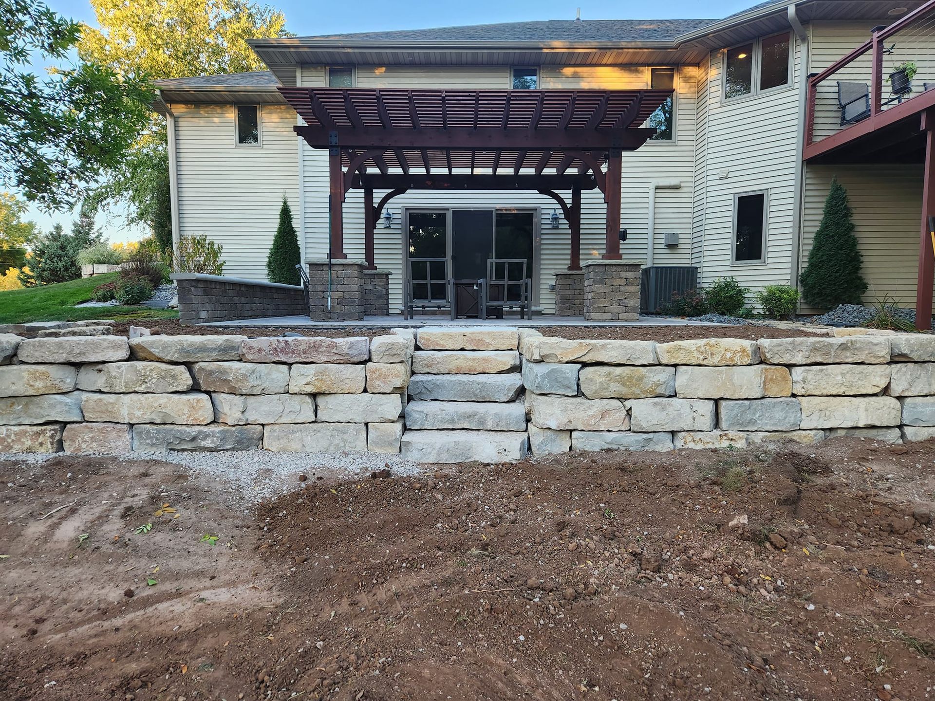 Backyard with stone retaining wall, steps, and pergola over patio doors.