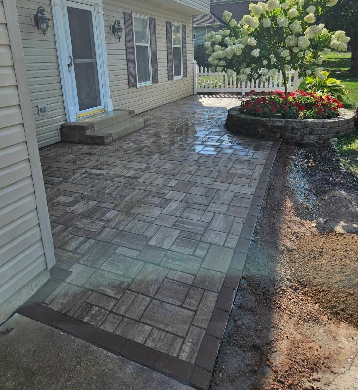 Brick patio with a planted flowerbed and house entrance.