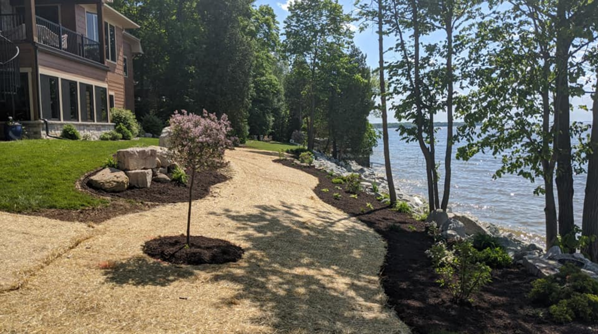 Pathway along a lake with a grassy lawn, trees, and a house on the left.