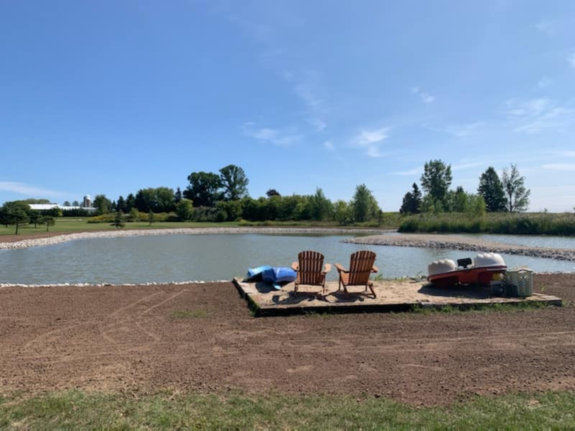 Lakeside dock with two wooden chairs, boats, and blue sky.