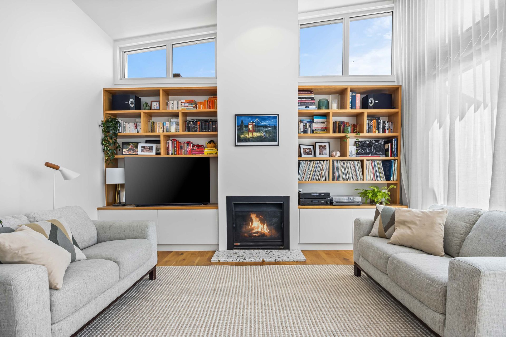 Cosy living space featuring built-in timber shelves, fireplace and natural light.