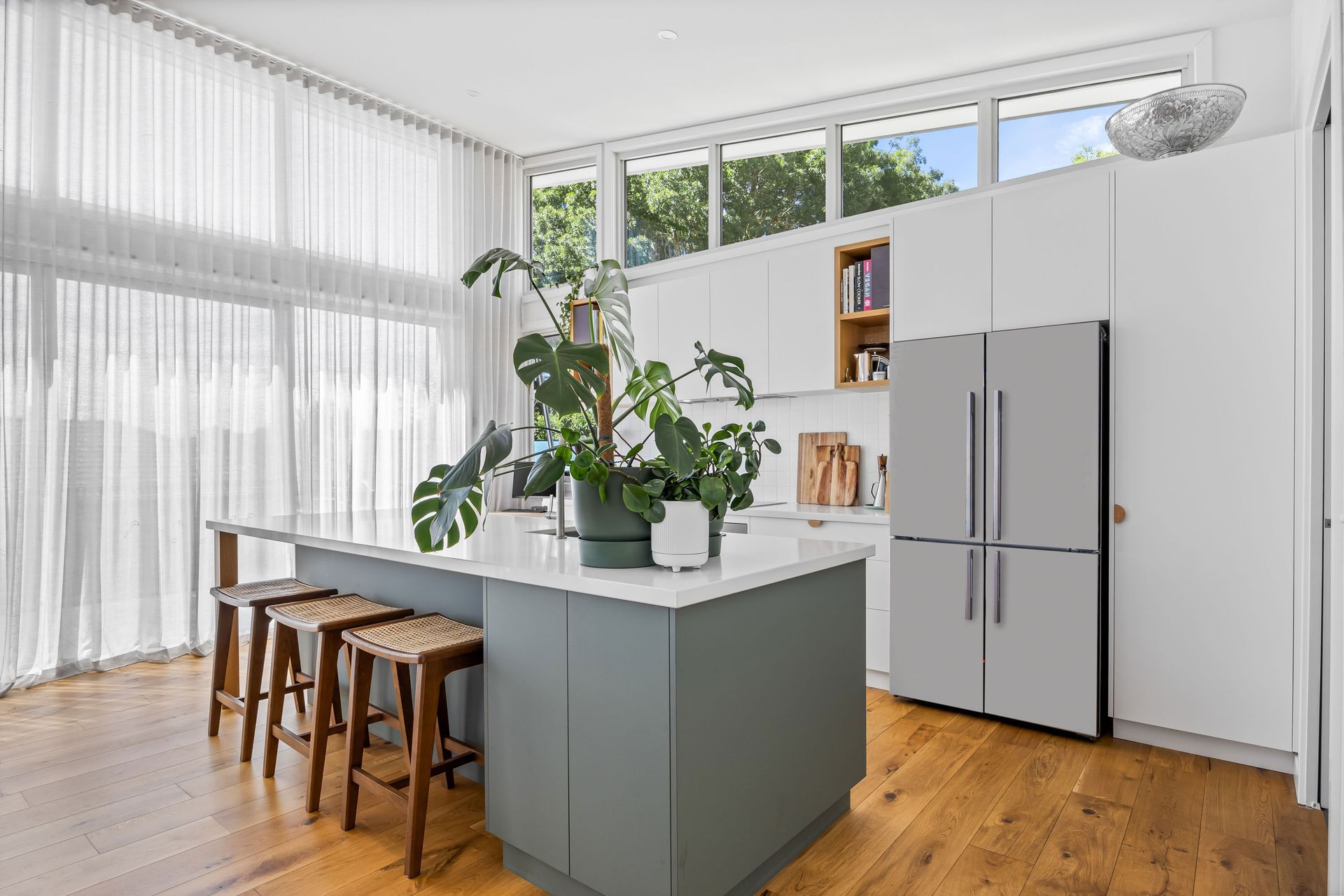 Spacious kitchen with green island, timber stools and sheer curtains.