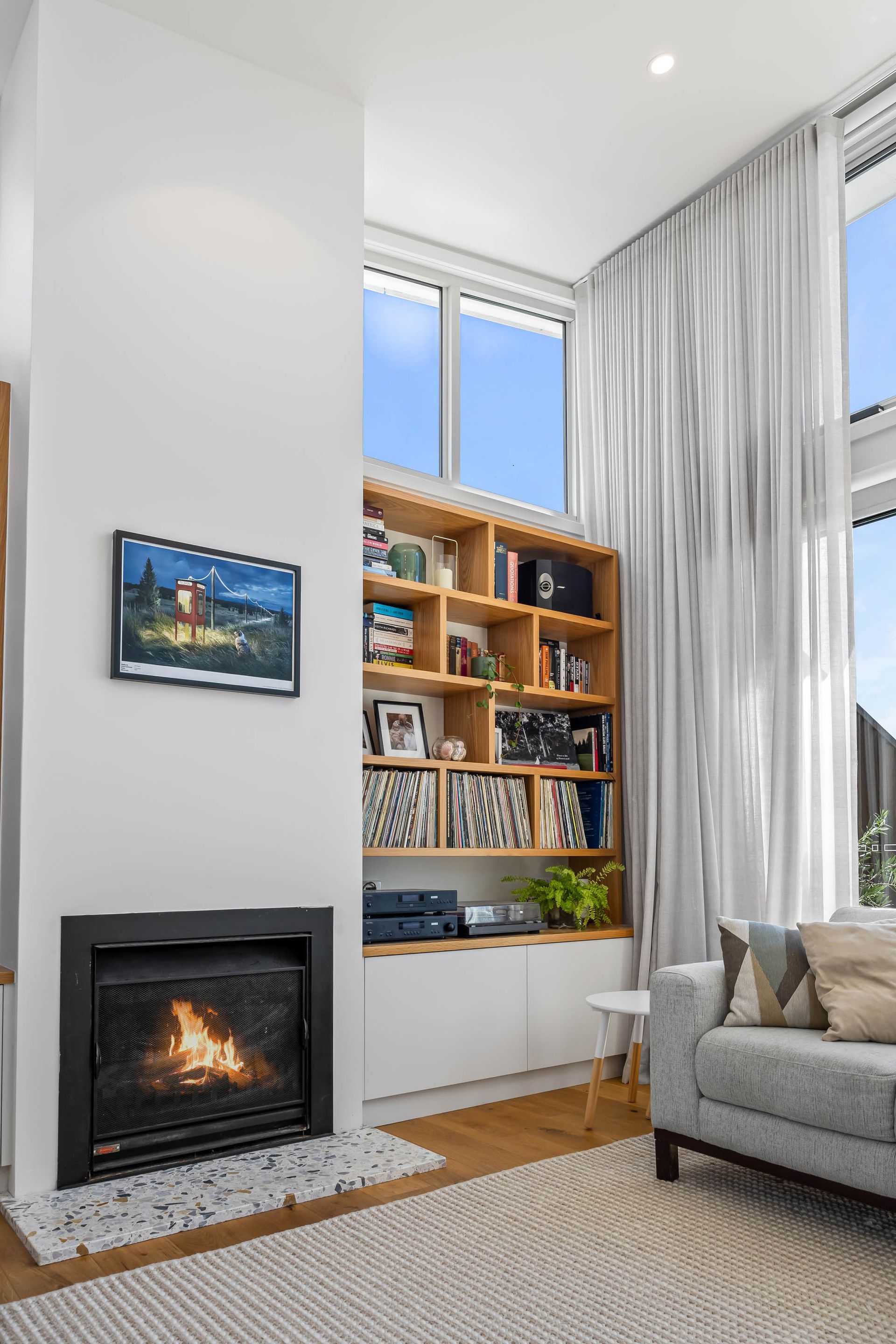 Tall feature fireplace with terrazzo hearth, built-in timber shelving and sheer double-height curtains