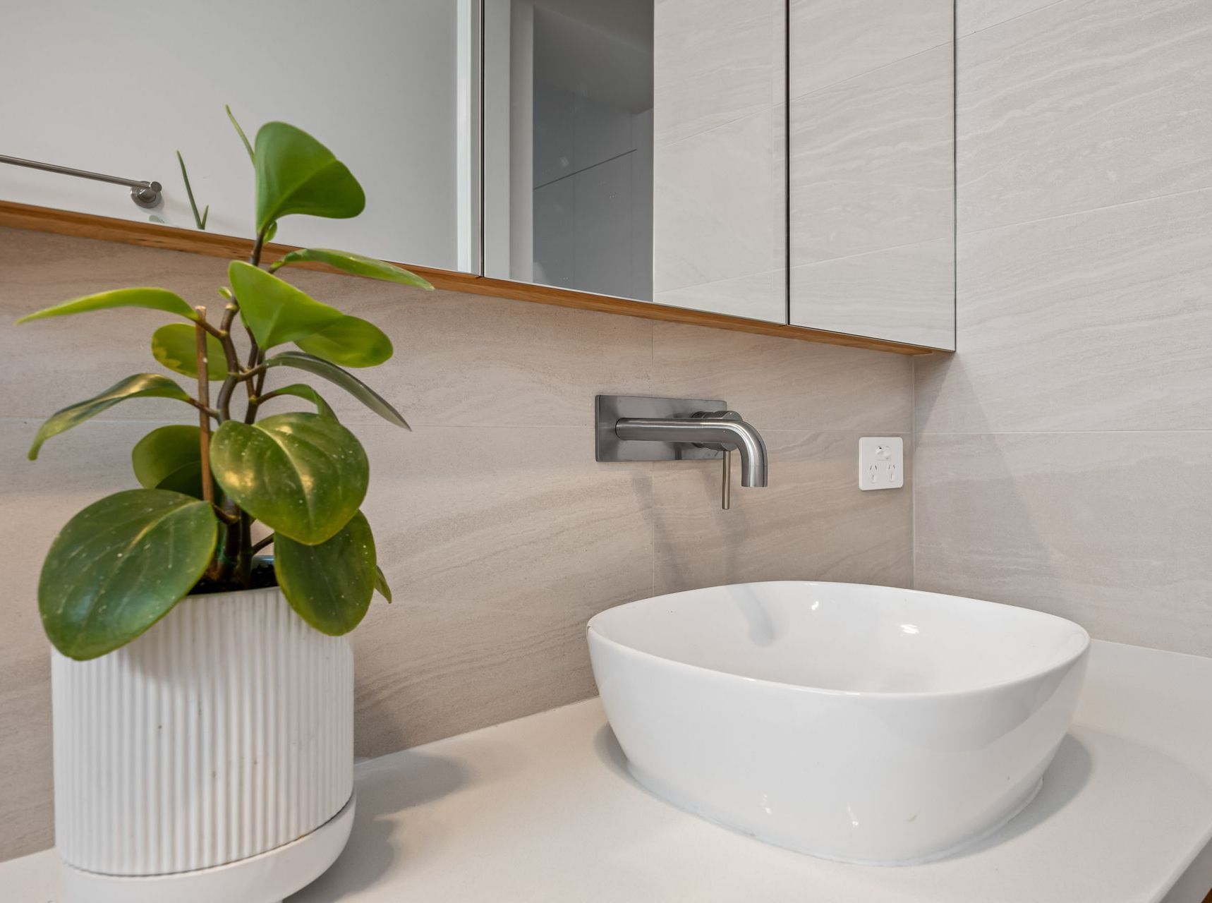 Stylish bathroom vanity with round basin, tapware and indoor plant.