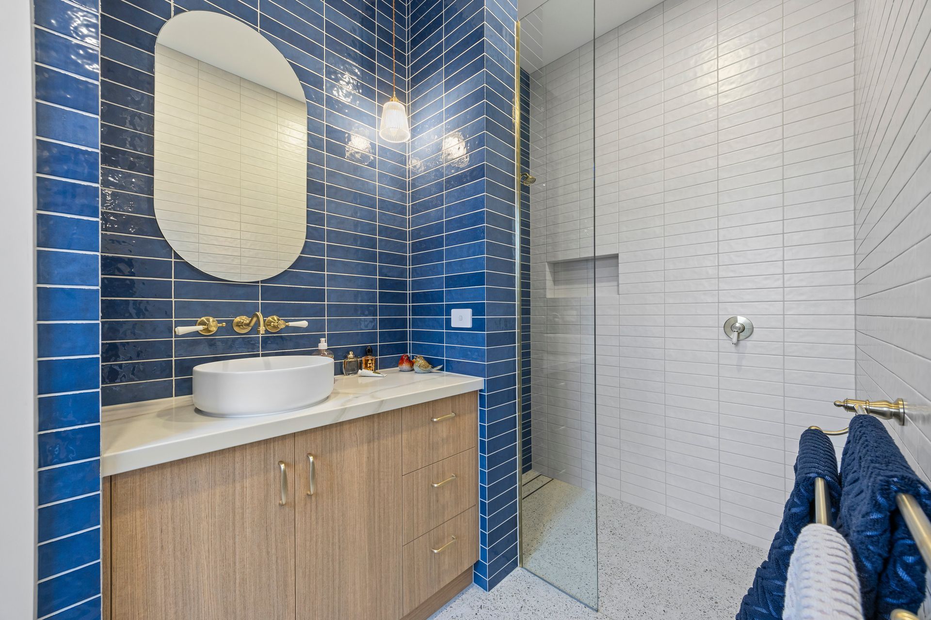 Navy tiled bathroom with brass tapware and oval mirror