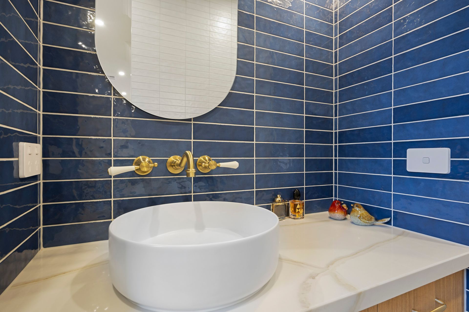 Navy tiled bathroom with brass tapware and oval mirror