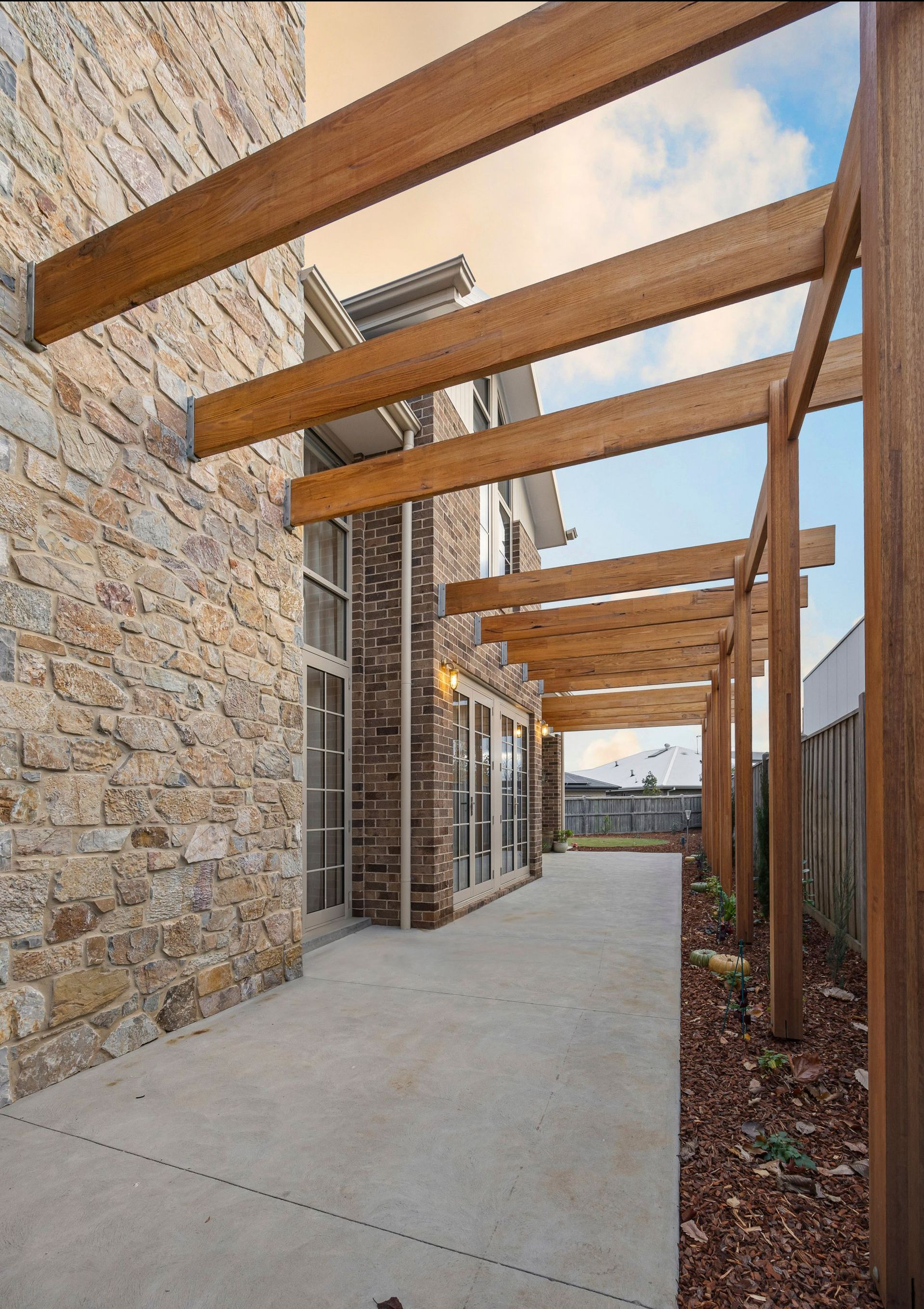 Stone-clad exterior with timber pergola and polished concrete path