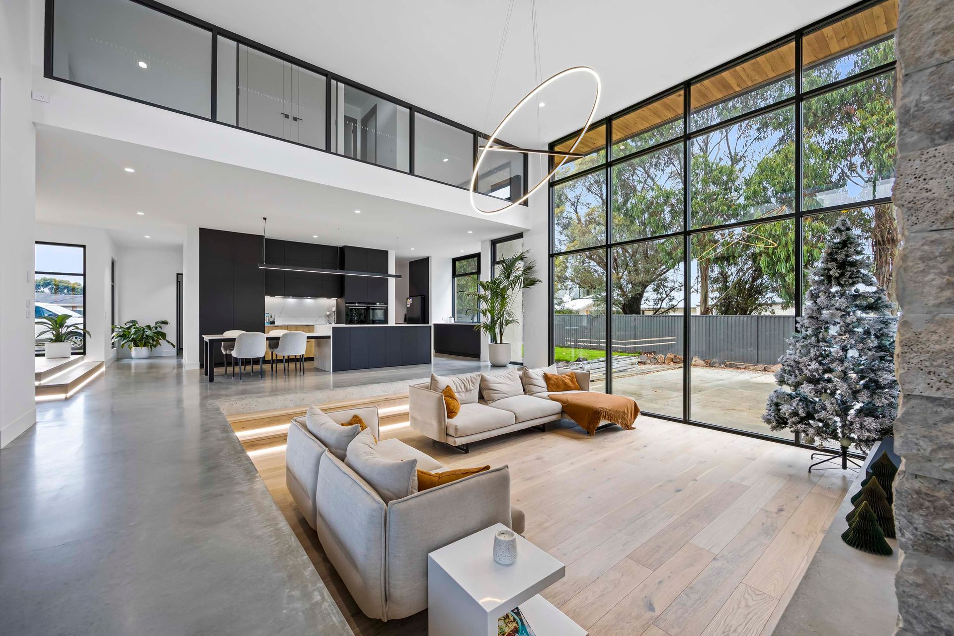Spacious open-plan living with double-height windows and a view into the modern kitchen and lounge.
