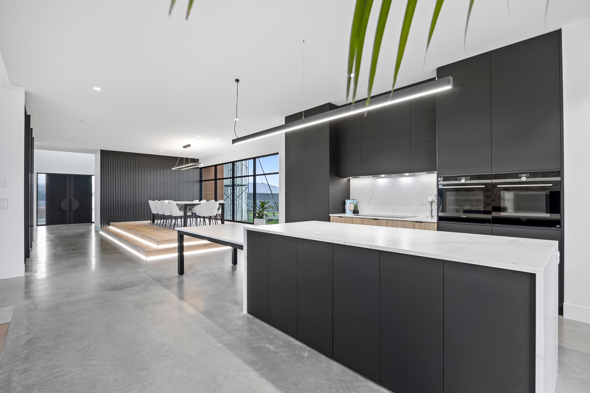 Minimalist kitchen with black island bench and concrete flooring.