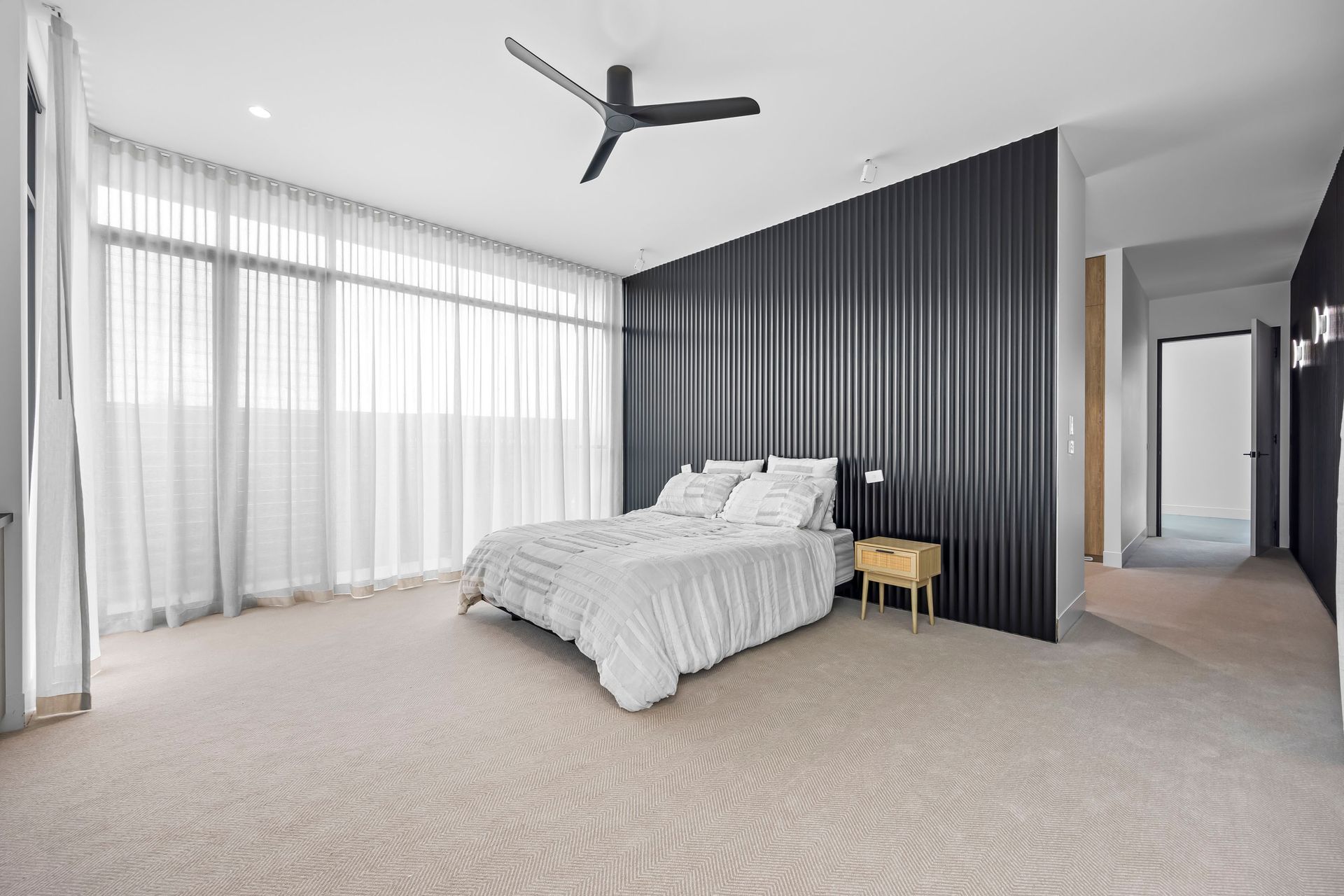 Master bedroom with full-length sheer curtains and textured black wall panelling.
