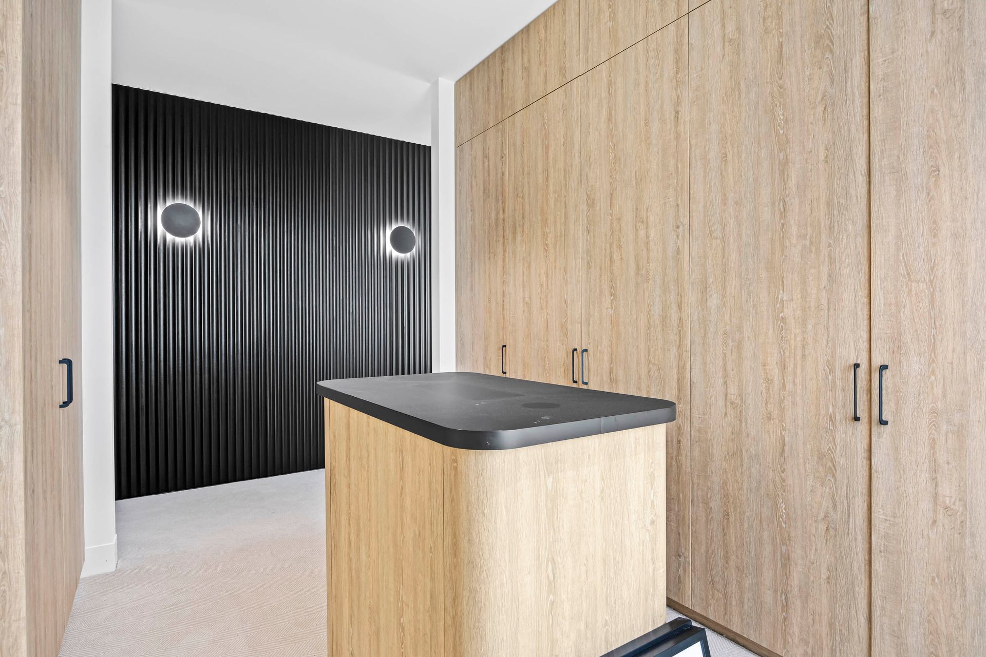 Walk-in robe with central timber island and dark feature wall.