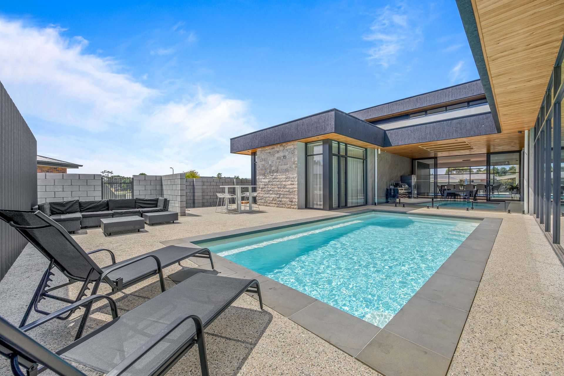 Outdoor pool surrounded by sun loungers and glass fencing.
