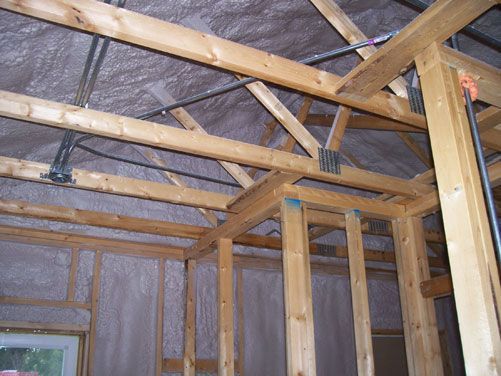 Unfinished room with exposed wooden ceiling joists and wall framing, insulated with plastic sheeting.