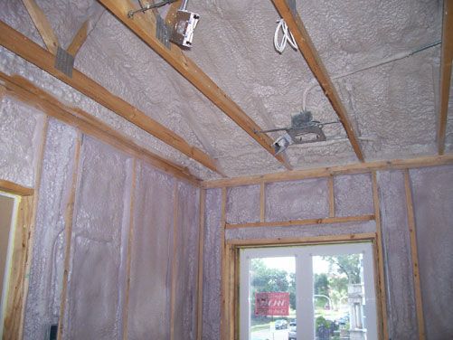 Interior wall and ceiling framing with exposed insulation and a window in a small room