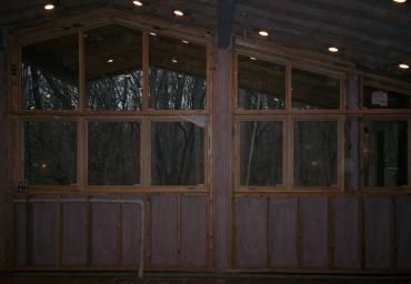 Wooden cabin porch with large windows and warm interior lights at night