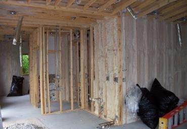 Unfinished framed interior of a house with exposed wood studs and construction materials on the floor.
