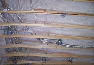 Exposed attic ceiling with wooden beams, foil insulation, and electrical wiring.