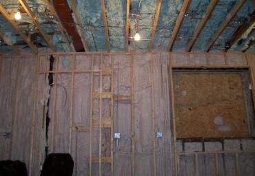 Interior wall under construction with exposed wooden studs, insulation, and unfinished ceiling beams
