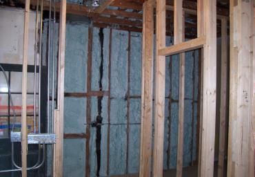 Interior wall framing with exposed studs and blue insulation in a partially finished room