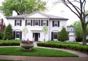 White two-story house with black shutters, manicured lawn, and flower planter in front yard