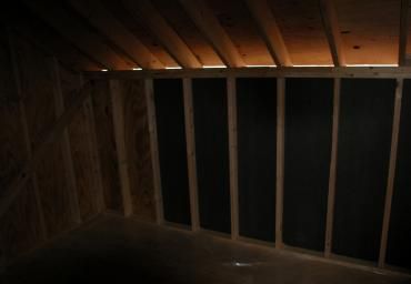 Dim attic interior with exposed wooden rafters and vertical framing against a dark opening
