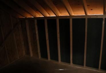 Dim attic with exposed wooden rafters and dark wall framing under low light.