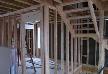 Unfinished house interior with exposed wooden framing and a ladder near a doorway.