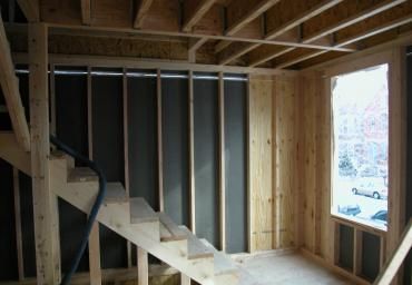 Unfinished interior with wooden stairs, exposed framing, and a large window opening to a snowy view.