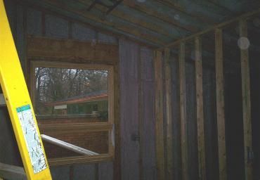 Partially framed room with a yellow ladder, window opening, and exposed wall studs