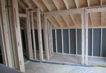 Unfinished room framing with exposed wooden studs, sloped ceiling, and dark insulation panels.