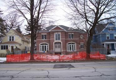 Row of houses with bare trees and orange construction fencing along a snowy street