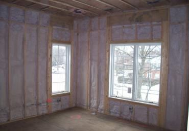 Unfinished room with exposed insulation and two windows showing a snowy street outside