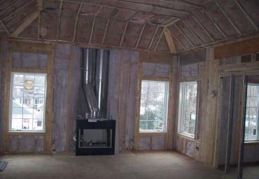 Unfinished room with exposed framing, windows on three sides, and a black fireplace in the center wall