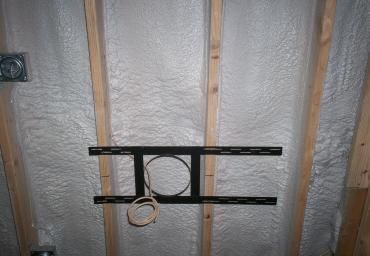 Black bracket with a coiled wire mounted on insulated wall studs.