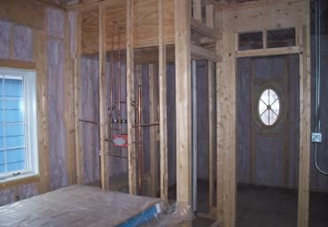 Unfinished interior framing with exposed studs, a window on the left, and a front door on the right.