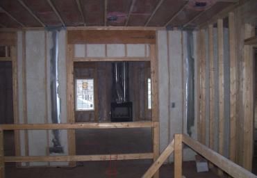 Unfinished interior room with exposed studs, wooden framing, and a doorway to a dim hallway.