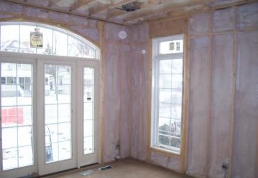 Unfinished room with arched glass doors and windows, exposed wall framing, and bare floor.