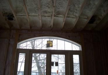 Dim interior with a large arched window and glass doors, showing exposed ceiling beams.