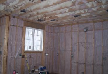 Unfinished room with exposed insulation, wooden framing, and a small window.