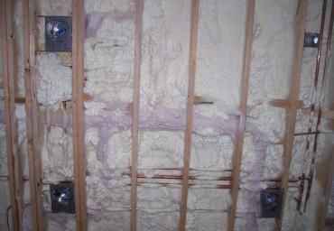 Insulated wall framing with exposed studs and white spray foam insulation.